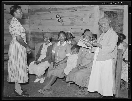 Juanita Coleman (Miss or Mrs.), teacher and NYA (National Youth Administration) leader, listening to one of her pupils in adult class read. She has just learned, is eighty-two years old and best in class. They meet in old church building for reading, writing, arithmetic, and general discussion and e