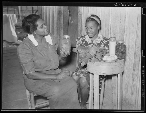 Nurse Shamburg gives Viola Pettway instructions and help about her diet in treatment of pellagra. She has been sick about four years and is a little better now. Her mother has thirteen children and twenty-five dollars a month for all. Table top is made from cheese box. Gee's Bend, Alabama