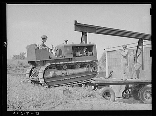 Loading repaired tractor from bank to truck ready to leave FSA (Farm Security Administration) warehouse depot in Atlanta, Georgia