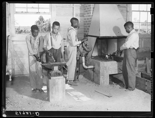 O.C. Cramer, Frederick West, J.W. West and another student sharpening plow point at forge in school shop. Flint River Farms, Georgia