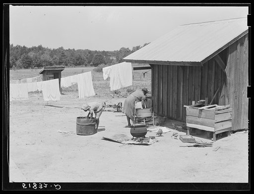 Lonny Smith's wife and daughter doing laundry by new smoke and washhouse in their yard. Flint River Farms