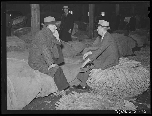 Farmers sitting around and talking inside tobacco warehouse while waiting for auction sale. Durham, North Carolina