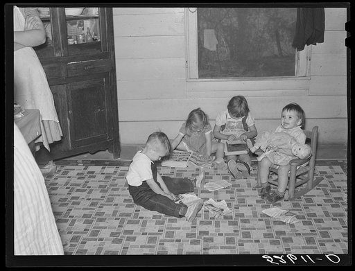 Children playing and cutting out pictures from Sears Roebuck catalogue on kitchen floor while their parents prepare dinner for the men on cornshucking day, at home of Mrs. Fred Wilkins. Tallyho, Stem, North Carolina. Granville County. See subregional notes (Odum) November 16, 1939