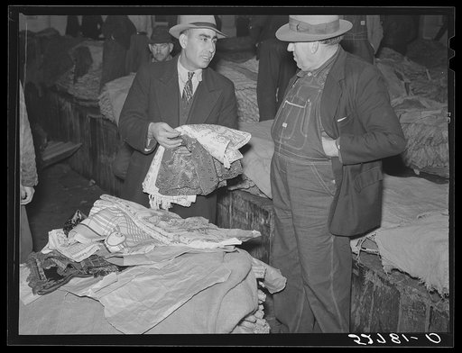 Farmers listening to Armenian bedspread, table linen, and shawl salesman in warehouse during tobacco auctions. Durham, North Carolina