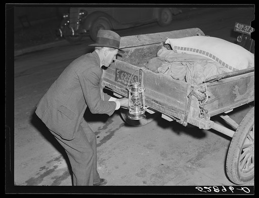 Mr. Elvin Wilkins fastening a new lantern on the back of his trailer in which he brought his tobacco to the warehouse for auction sale. He is returning home with a bag of hog feed in the trailer. Durham, North Carolina