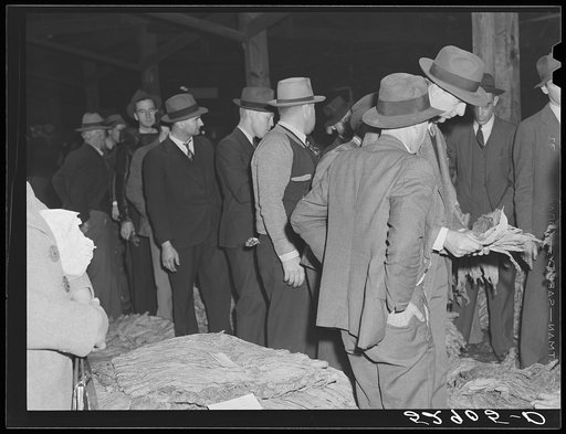 Mr. Elvin Wilkins watching while the buyer examines his tobacco at auction sale in warehouse in Durham. Durham County, North Carolina