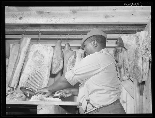 Lewis Wiggins cutting off a slice of homecured ham in his smokehouse. La Delta Project, Thomastown, Louisiana