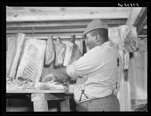 Untitled photo, possibly related to: Lewis Wiggins cutting off a slice of homecured ham in his smokehouse. La Delta Project, Thomastown, Louisiana