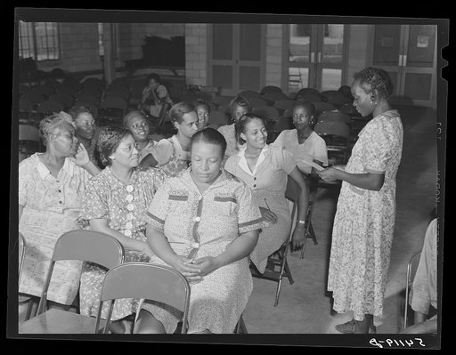 One of the camp members, vice-president of women's club, reading suggestions to group for future planning and discussions. Home management supervisor Corinne Williams sitting opposite her, encourages the members to conduct and participate in their own meeting. Assembly building at Okeechobee migrato