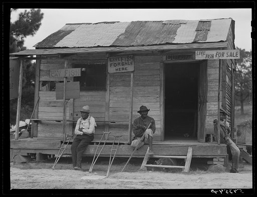 Untitled photo, possibly related to: Natchitoches, Louisiana. A Negro sitting on the porch of a store where live fish are for sale