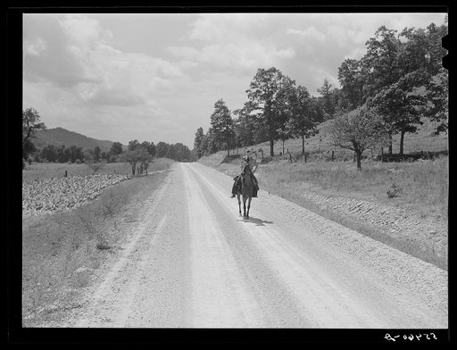 Rural mailman riding to the crossroads where he will meet another postman in a wagon. The mail sacks will then be transferred to his saddlebags and he will take the mail further up the side road and creek beds where no wagon or car can go. In the mountain section near Morehead, Kentucky
