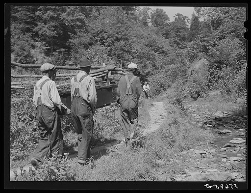 Mountain people carrying a coffin up the creek bed to the family graveyard where it will be buried. This section is too isolated to have a formal funeral service immediately. Up South Fork of the Kentucky River, Kentucky