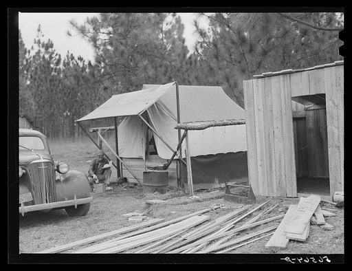 Camp Livingston construction worker cooking outdoors in front of shack which he built out of lumber he purchased or found nearby. This is along main highway on government property so he does not have to pay rent. Water is hauled from a nearby church faucet as there are no sanitary facilities. Alexan