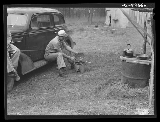 Untitled photo, possibly related to: John H. Poole, Jr. cooking while sitting on side of car. He is a carpenter on construction job at Camp Livingston. He comes from Monroe, Louisiana, where he has an electrical shop