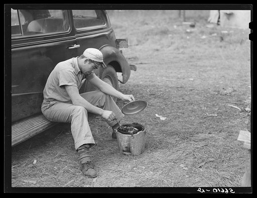 John H. Poole, Jr. cooking while sitting on side of car. He is a carpenter on construction job at Camp Livingston. He comes from Monroe, Louisiana, where he has an electrical shop
