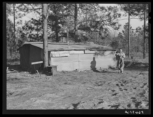 Construction workers' shack on government property off new highway to flying field which is also in the making. Living quarters of gravel pit workers and truck drivers. Ten to twelve men are housed and fed in this shack, which was built by the group who occupy same. Name of shack is Texas Long Horns