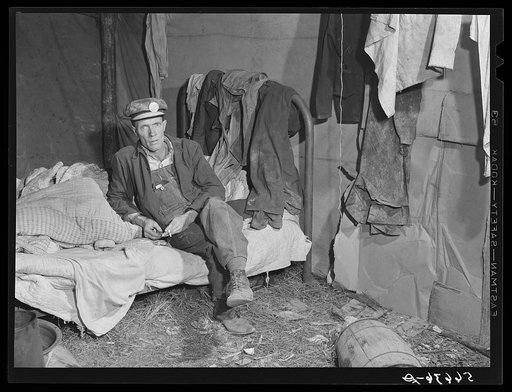 Interior of shack described in other pictures. Mr. W.R. Carpenter of Beaumont, Texas also a truck driver, seated on bed. Men very willing to have photo made, saying they should cooperate in this undertaking as they were all free Americans and hoped for better conditions. Alexandria, Louisiana