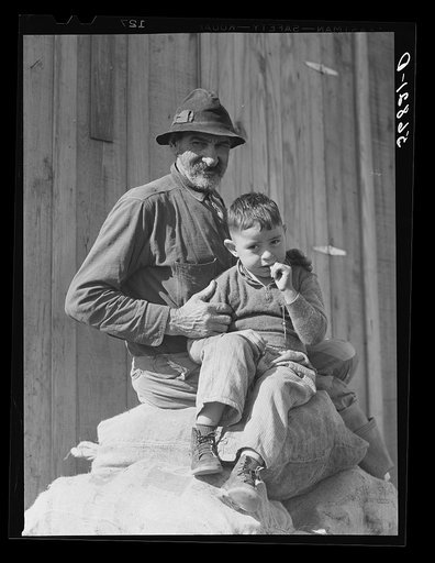 Spanish muskrat trapper and his grandson sitting on sacks of dried muskrat pelts, in front of their camp in the marshes. Delacroix Island, Saint Bernard Parish, Louisiana