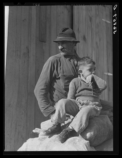 Untitled photo, possibly related to: Spanish muskrat trapper and his grandson sitting on sacks of dried muskrat pelts, in front of their camp in the marshes. Delacroix Island, Saint Bernard Parish, Louisiana