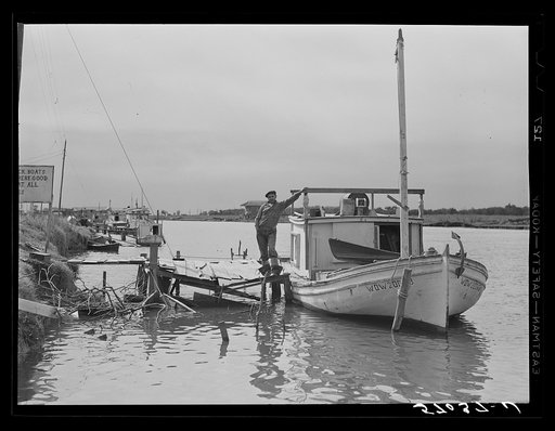 Spanish muskrat trapper standing beside his boat used to go out of the camp in the marshes and for fishing in other seasons. Delacroix Island, Louisiana. See general caption number one