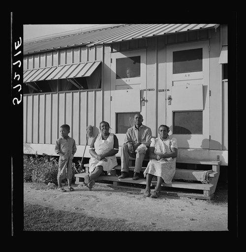 Migratory laborers sitting in front of their metal shelter at Okeechobee migratory labor camp. Belle Glade, Florida