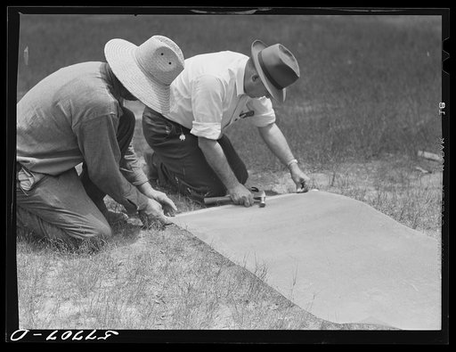 Fastening 16-mesh galvanized wire screen to battens before applying to open window frame. Screening demonstration. Charles County, La Plata, Maryland