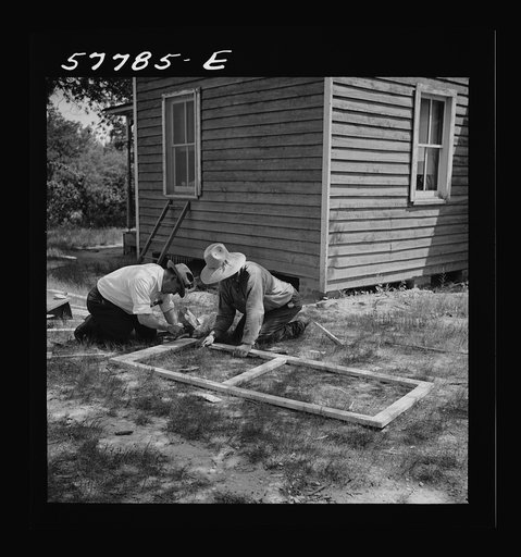 Screen door stock assembled and held together with corrugated fasteners.  Metal reinforcement strips are being nailed at corner joints on the outside of the frame. Charles County, La Plata, Maryland. Screening demonstration