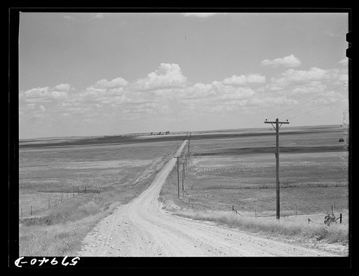 Road with Homestead, Montana, and grain elevators on the horizon