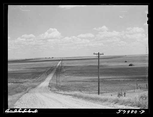 Road with Homestead, Montana, and grain elevators on the horizon