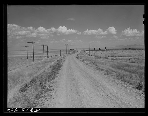 Road to Portage, Montana, with stacks of wheat and grain storage elevators in distance on right