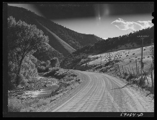 Road along Frying Pan Creek with stacks of wheat on the hillside. This is an excellent fishing area. Near Meredith, Colorado
