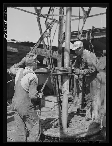 Oil workers pulling up old pipe to change bit on drilling pipe at bottom of oil well in C.C. Graber pool of Continental oil company. Moundridge area near McPherson, Kansas