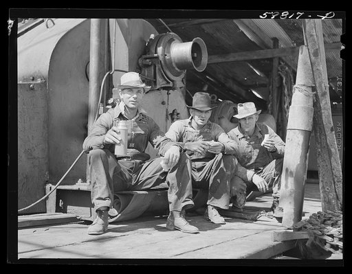 C.L. Saxton, driller; J.G. Betz, Cathead man; and L.C. Westerman, eating lunch around oil well in C.C. Graber pool of Continental oil company. Moundridge area near McPherson, Kansas