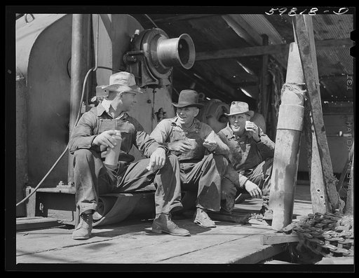 C.L. Saxton, driller; J.G. Betz, Cathead man; and L.C. Westerman, eating lunch around oil well in C.C. Graber pool of Continental oil company. Moundridge area near McPherson, Kansas