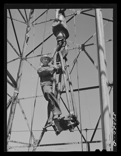 Driller C.L. Saxton, riding on traveling block to the top of oil well derrick. He was originally from Oklahoma, but has been in Kansas for last six years. Oil well in C.C. Graber pool of Continental oil company. Moundridge area near McPherson, Kansas