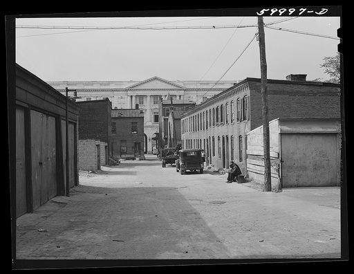 Schoots Court with Senate building in background. Four very small dark rooms rent for fifteen and eighteen dollars per month with water and privy in yard. It used to rent for six and eight dollars. Frank Coles and his friend are sitting on the bench He was a cement plasterer but has been on relief d