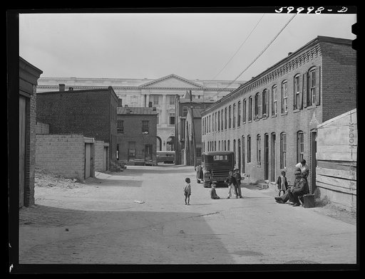 Schoots Court with Senate building in background. Four very small dark rooms rent for fifteen and eighteen dollars per month with water and privy in yard. It used to rent for six and eight dollars. Frank Coles and his friend are sitting on the bench He was a cement plasterer but has been on relief d