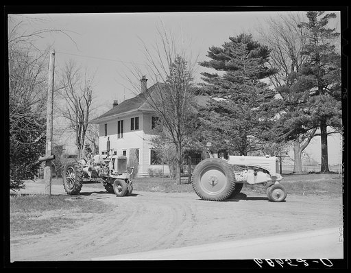 Father and son driving tractors out of the farmyard to a piece of land a mile down the highway where they will disc and plow. Grundy County, Iowa