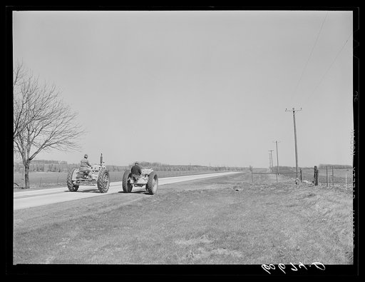 Father and son drive tractors a mile down the road to a field which belongs to them. They are breaking down stalks and plowing. Grundy County, Iowa