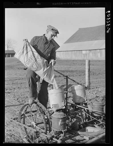 Pouring fertilizer into box on corn planter. Jasper County, Iowa