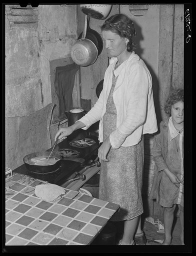Mother of five children preparing evening meal. They live in an abandoned house on property of fruit grower. Berrien County, Michigan