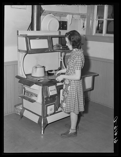 Farm girl putting wood in kitchen stove. Meeker County, Minnesota