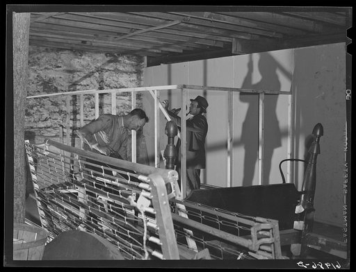 Workmen building a room in the basement of Mr. Tilly's furniture store; secondhand beds and stoves, etc. which have been moved out in the foreground. Radford, Virginia