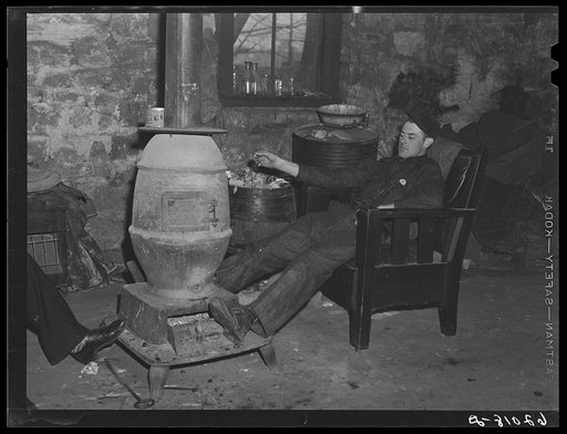 Construction worker by stove in basement of secondhand furniture store. The owner of this store often lets men sit around all night when they are unable to find a room to rent. Radford, Virginia
