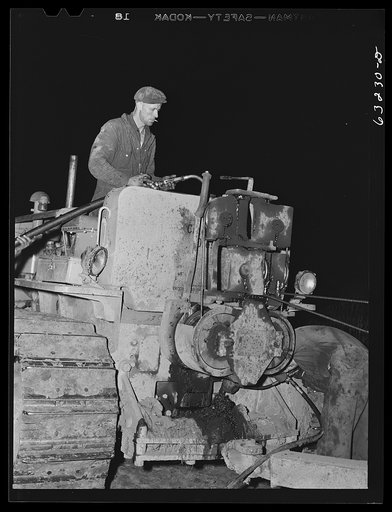 Untitled photo, possibly related to: Member of road construction gang greasing "cats" at night. Grant County, Wisconsin