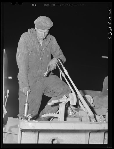 Untitled photo, possibly related to: Member of road construction gang greasing "cats" at night. Grant County, Wisconsin