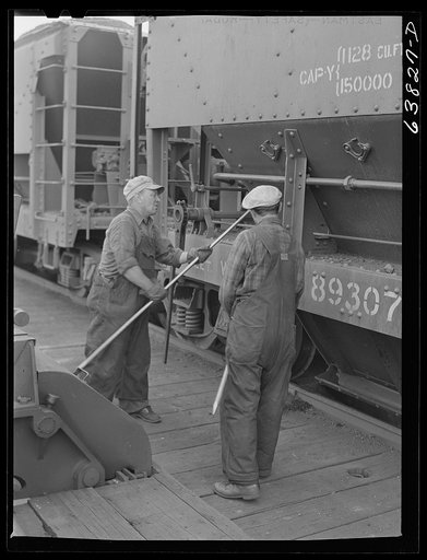 Ore punchers knocking side of car after it has been opened to let iron ore fall into bin where it is stored before being loaded onto boat. Allouez, Wisconsin