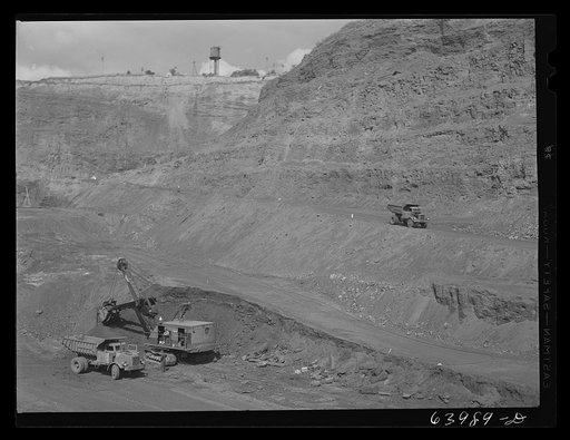 Loading trucks with iron ore at the Albany mine, Hibbing, Minnesota. This mine formerly used railroad until trucks were found more economical; they can climb the steep grade in much shorter time