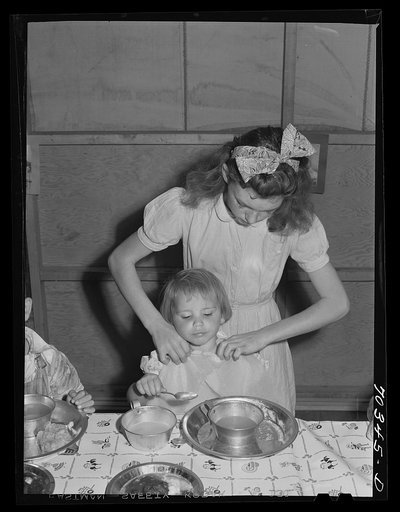 Lunch at the nursery school at the FSA (Farm Security Administration) mobile camp for migratory farm workers , Odell, Oregon. The older girl, member of the Junior Campers League receives credits for helping in the nursery school