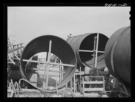 Segments of penstock pipe which will be used to transport water from reservoir formed by Shasta Dam to hydroelectric turbines. Notice the worker on top pipe; he is welding segments together. Shasta County, California